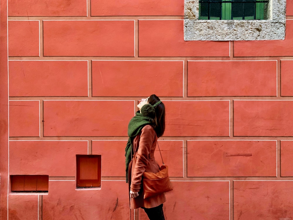 pessoa na jaqueta de couro marrom em pé na frente da parede de tijolo marrom