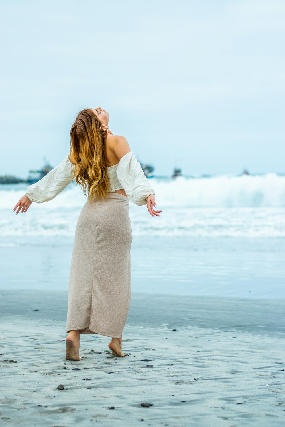 Mujer en vestido blanco de manga larga de pie en la playa durante el día