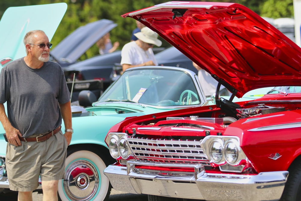 man in black t-shirt standing beside red car during daytime