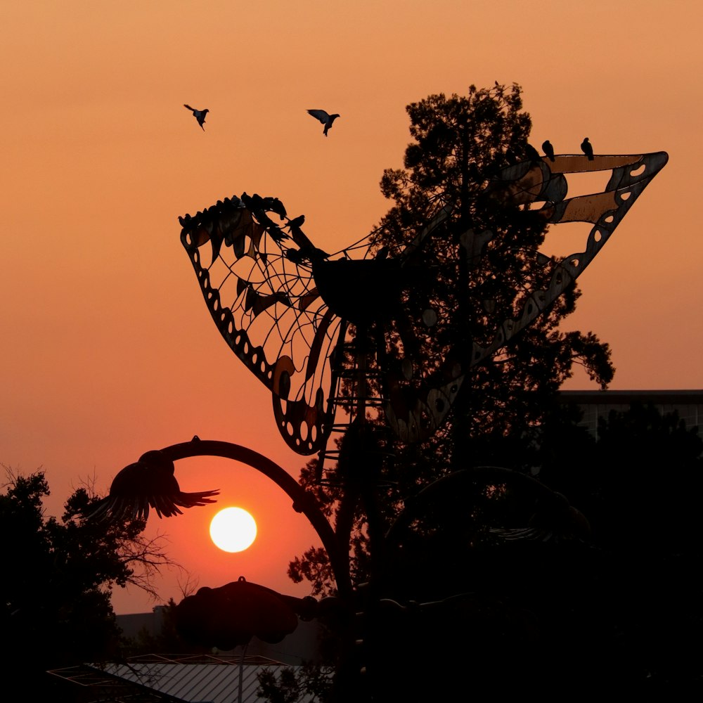 Silhouette von Vögeln, die während des Sonnenuntergangs über den Baum fliegen