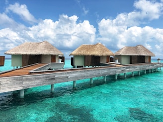 Overwater bungalows with wooden decks stretching over crystal-clear blue lagoons under a bright sky.