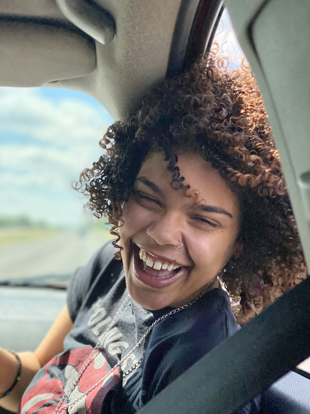 smiling woman in gray shirt sitting inside car during daytime