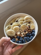 person holding white ceramic bowl with white and blue berries