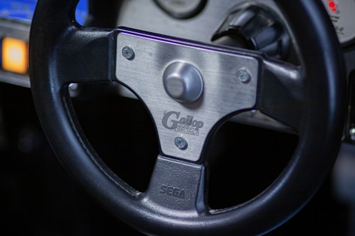 A close-up of a sleek simracing steering wheel with the Pit Stop Racer logo illuminated in yellow.