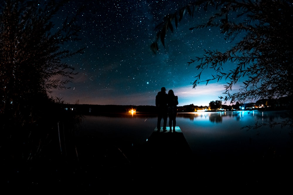 Silhouette von Mann und Frau, die nachts auf dem Dock stehen