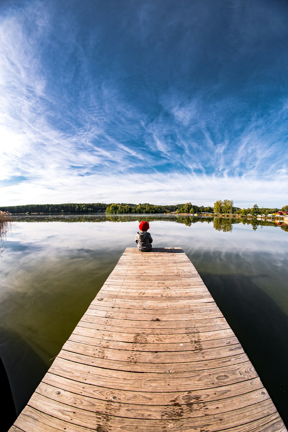 Una persona sentada en un muelle en medio de un lago