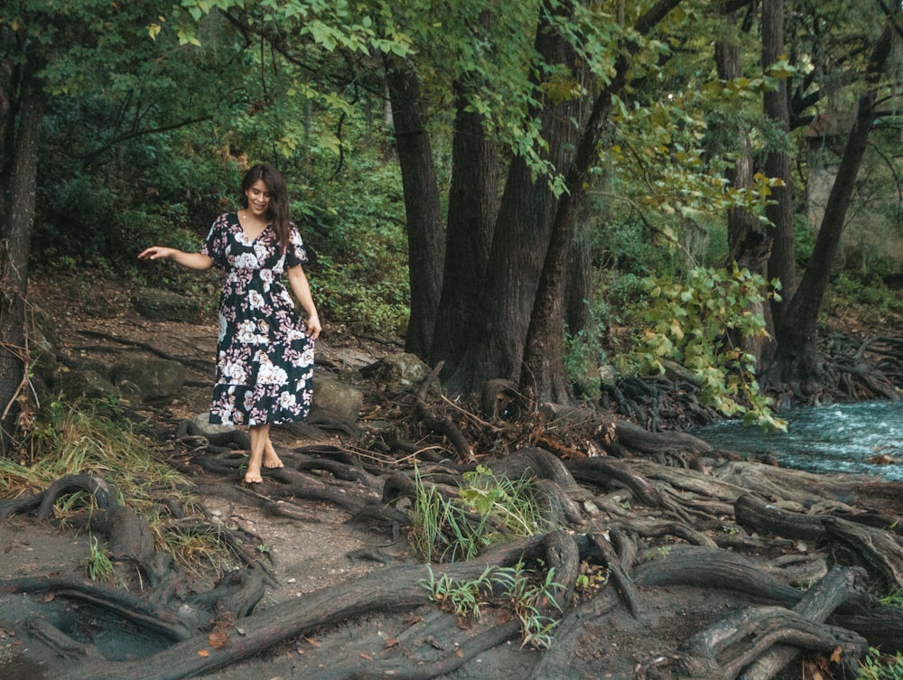 woman in black and white floral dress standing on brown tree log during daytime