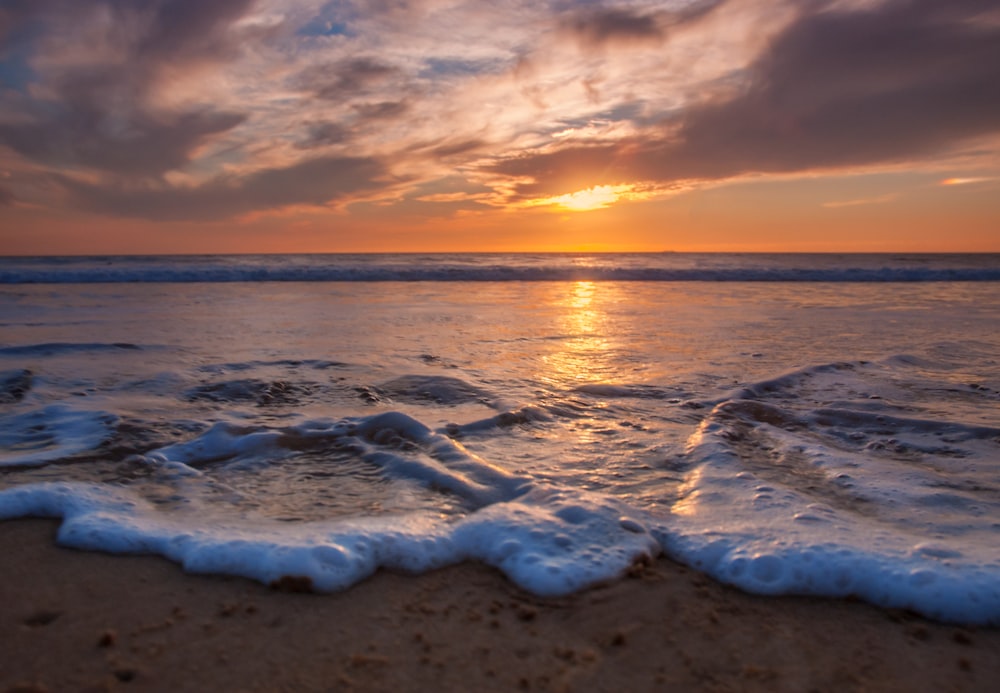 ocean waves crashing on shore during sunset