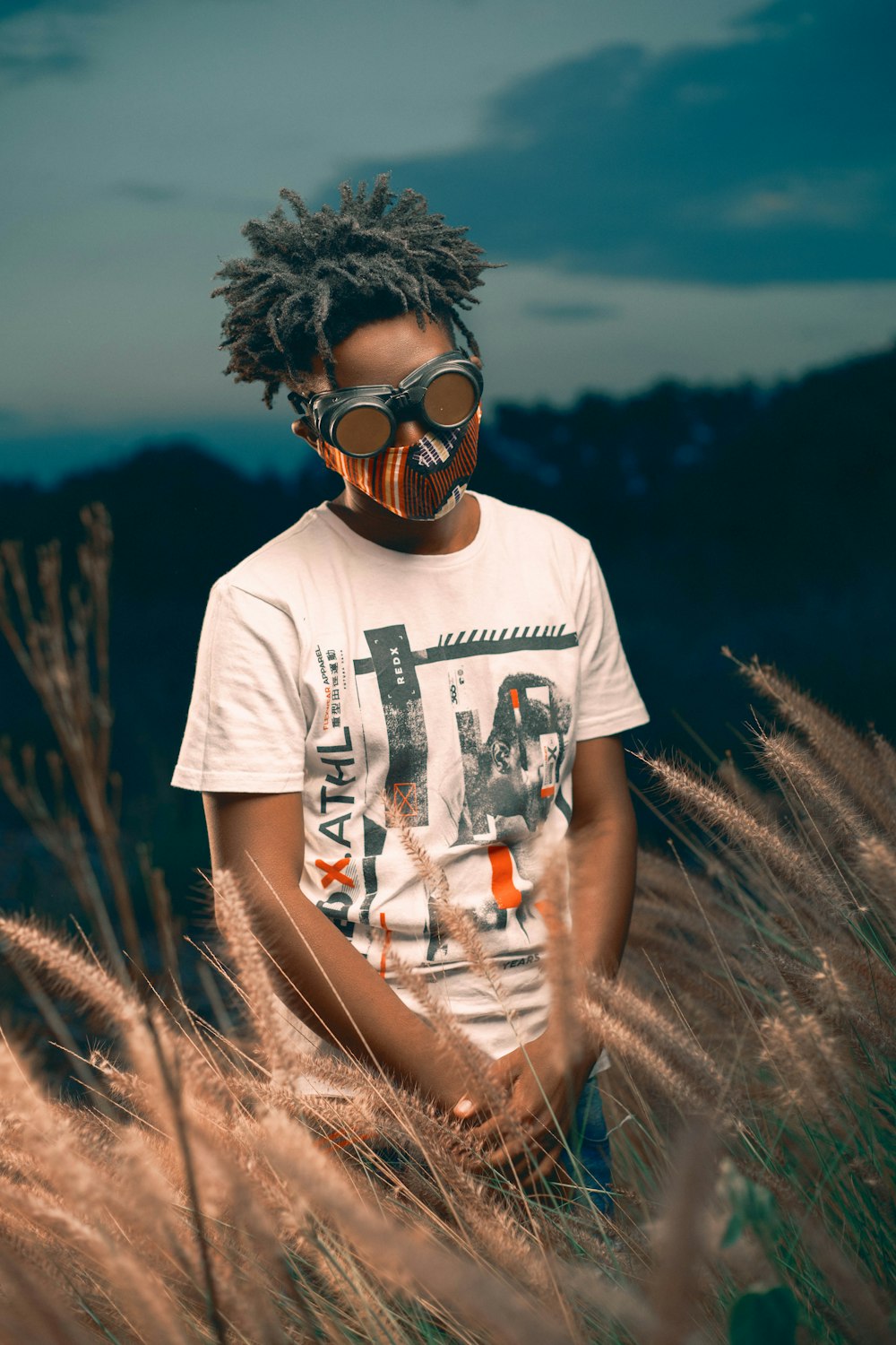 man in white crew neck t-shirt wearing black goggles standing on brown grass field during