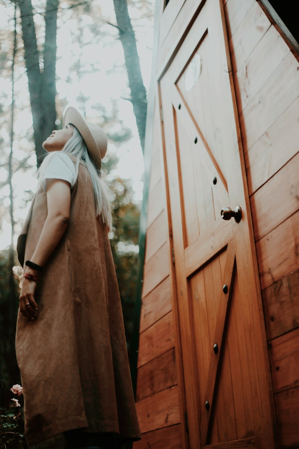 woman in brown sleeveless dress wearing white sun hat standing beside brown wooden door during daytime