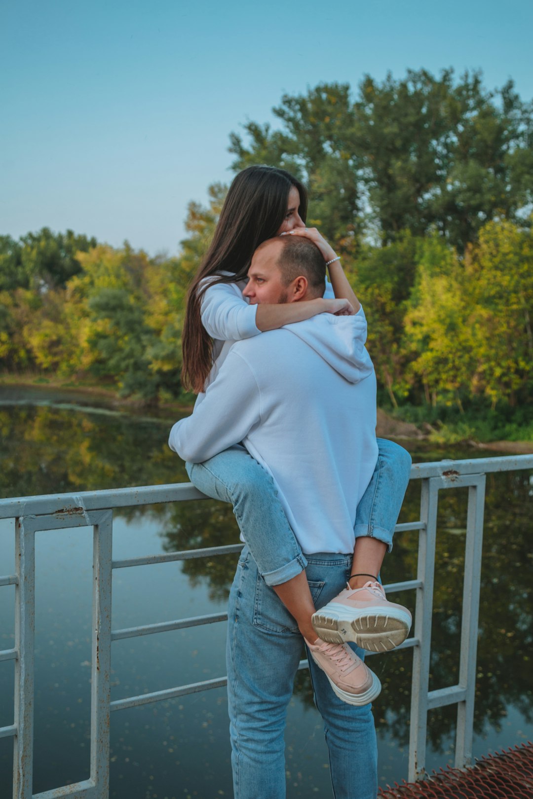 woman in white sweater and blue denim jeans standing on white wooden bridge during daytime