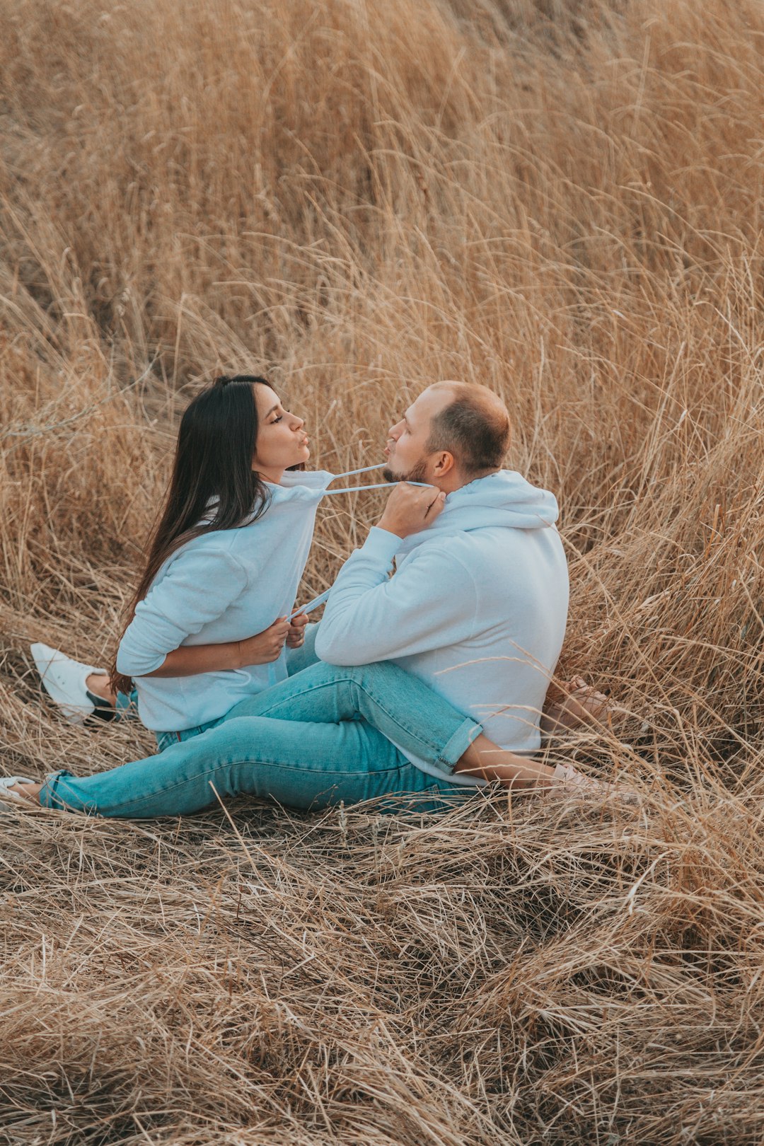 woman in white long sleeve shirt and blue denim jeans sitting on brown grass field