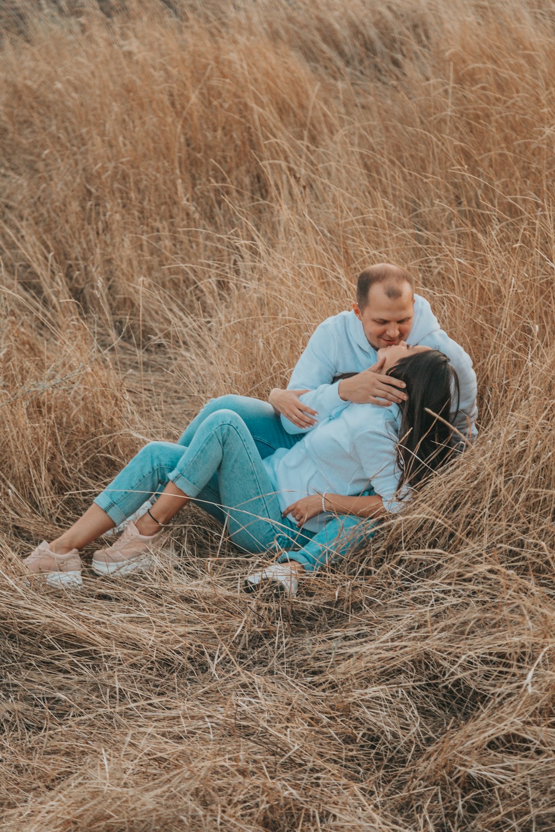 man in white shirt and blue denim shorts sitting on brown grass field