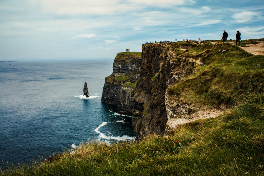 a group of people standing on top of a cliff next to the ocean