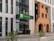 An entrance to a modern hotel building with a prominent brick wall feature. The hotel sign displays 'Holiday Inn' in green letters. Large glass windows are visible, and several potted plants decorate the area around the entrance. The building incorporates both contemporary and historical architectural elements.
