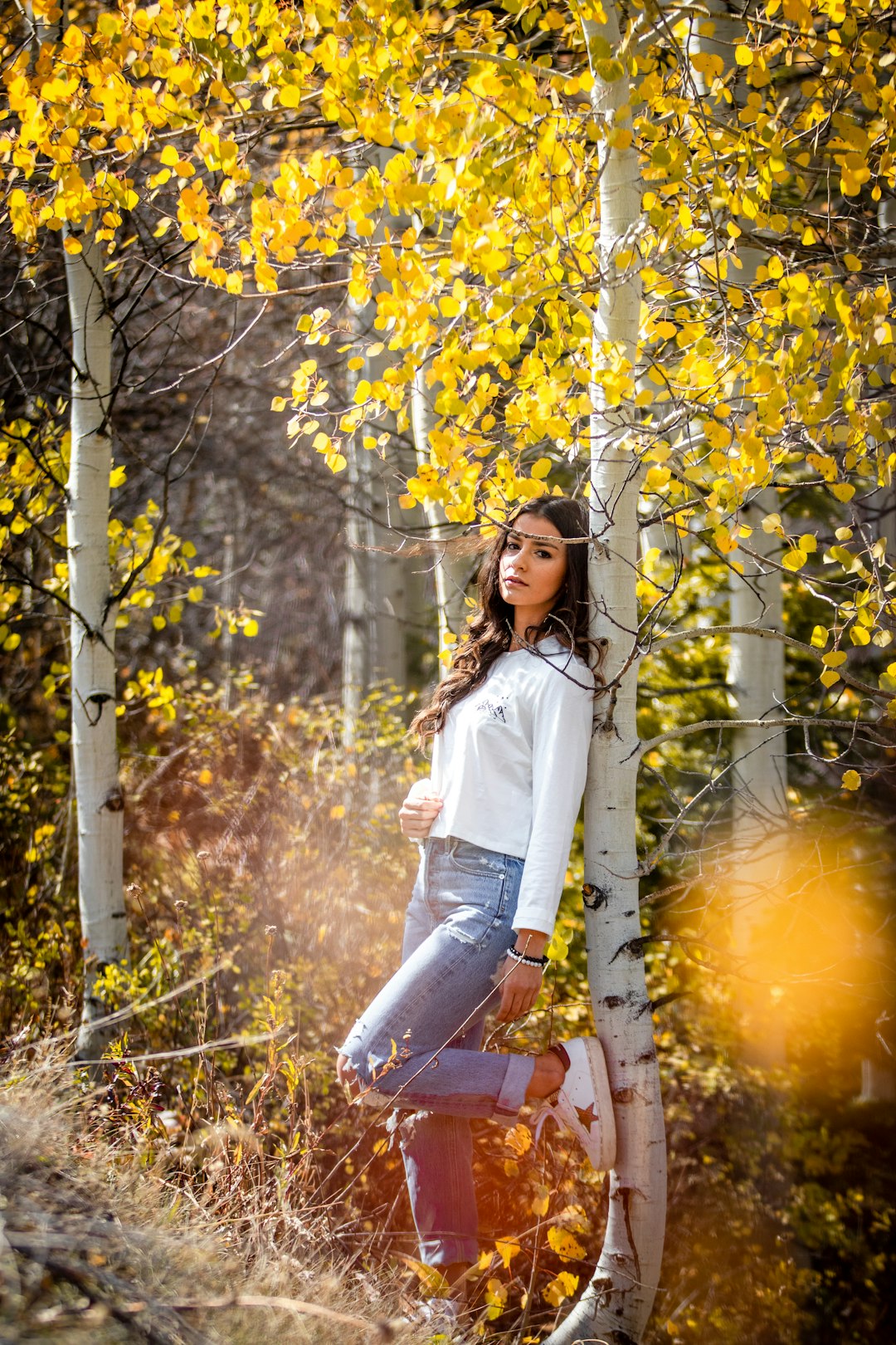 woman in white long sleeve shirt and blue denim jeans standing beside tree during daytime