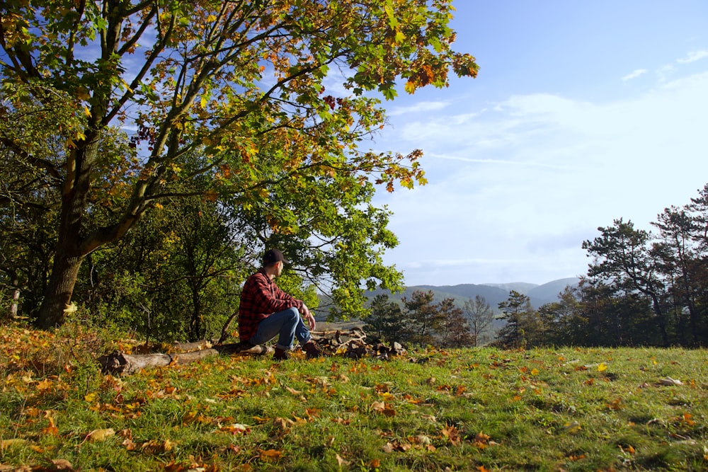 man in red and black jacket sitting on green grass field during daytime