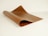 A rolled sheet of brown leather is placed on a white surface, showcasing its texture and flexibility. The lighting highlights the smooth yet slightly textured finish of the leather.