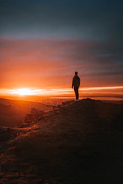 man in black jacket standing on brown rock during sunset