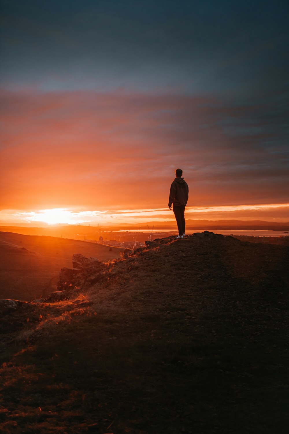 homme en veste noire debout sur le rocher brun pendant le coucher du soleil