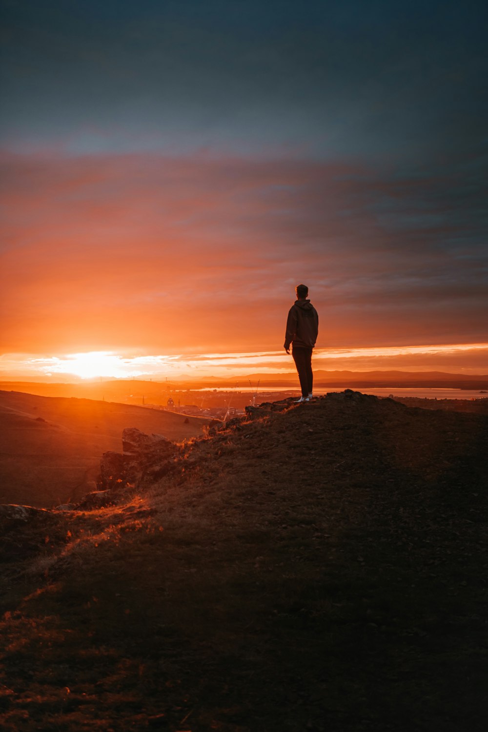 uomo in giacca nera in piedi sulla roccia marrone durante il tramonto