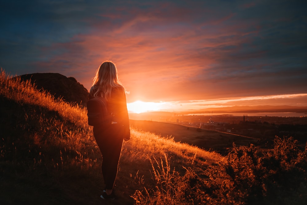 Frau in schwarzer Jacke steht bei Sonnenuntergang auf Rasen
