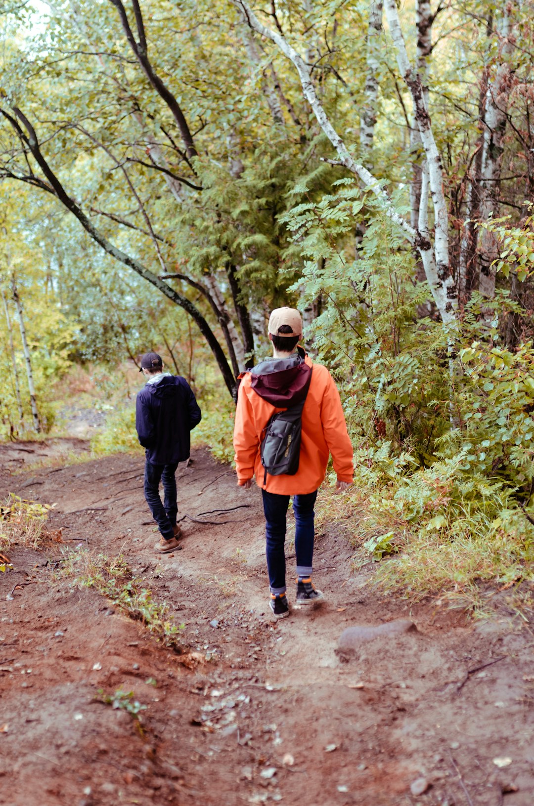 man in black jacket walking on dirt road between trees during daytime