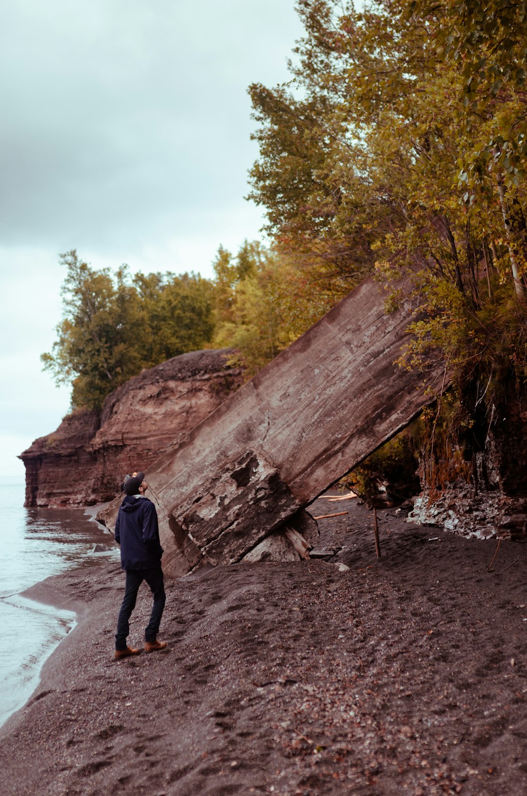 man in black jacket standing on brown rock near body of water during daytime