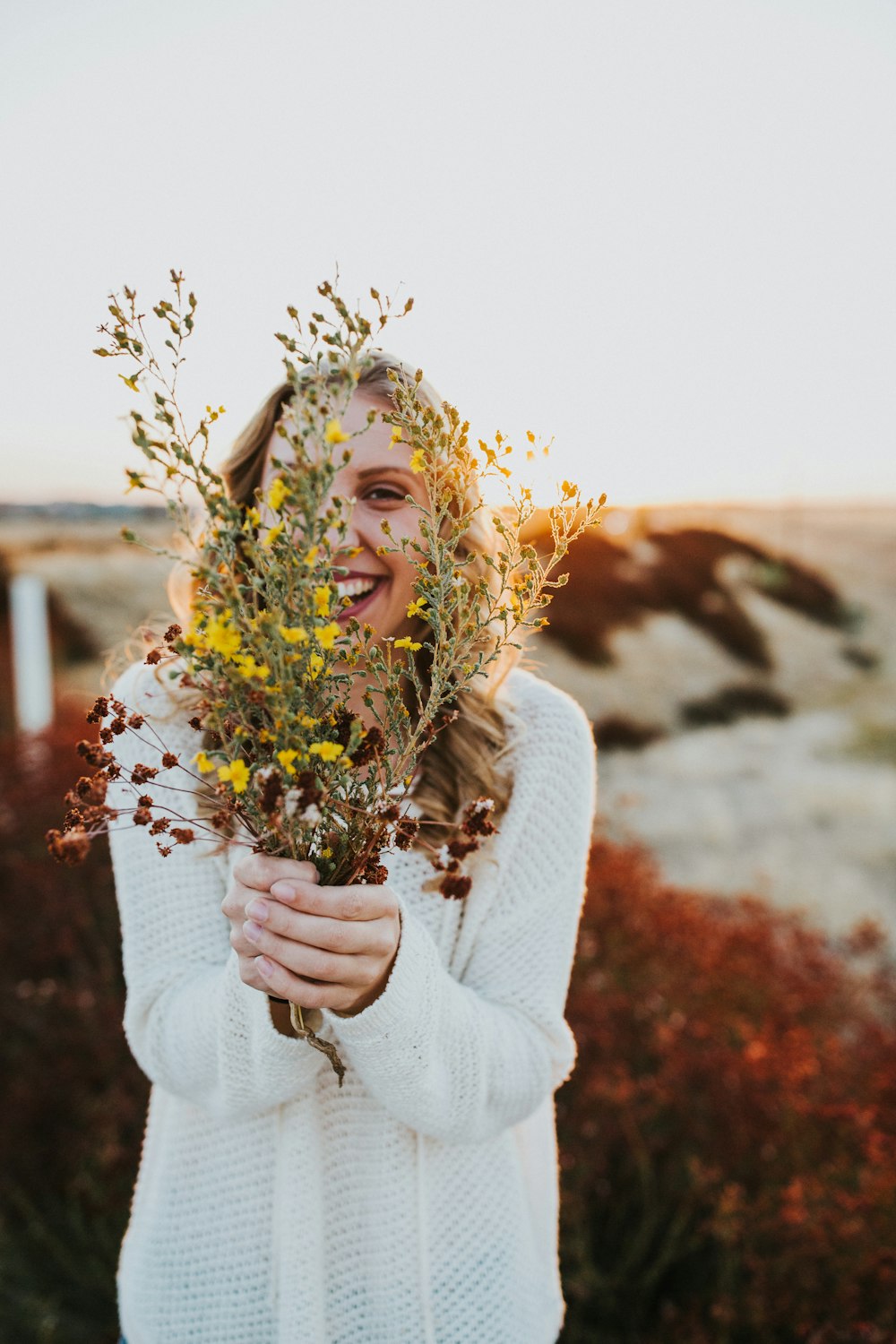 mulher no suéter branco que segura as flores amarelas