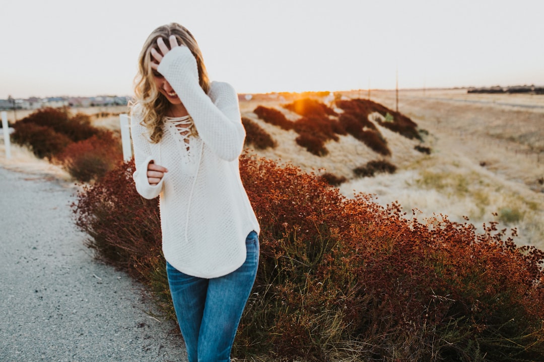 woman in white long sleeve shirt and blue denim jeans standing on gray asphalt road during