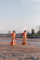 2 women walking on brown sand near body of water during daytime