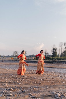 2 women walking on brown sand near body of water during daytime
