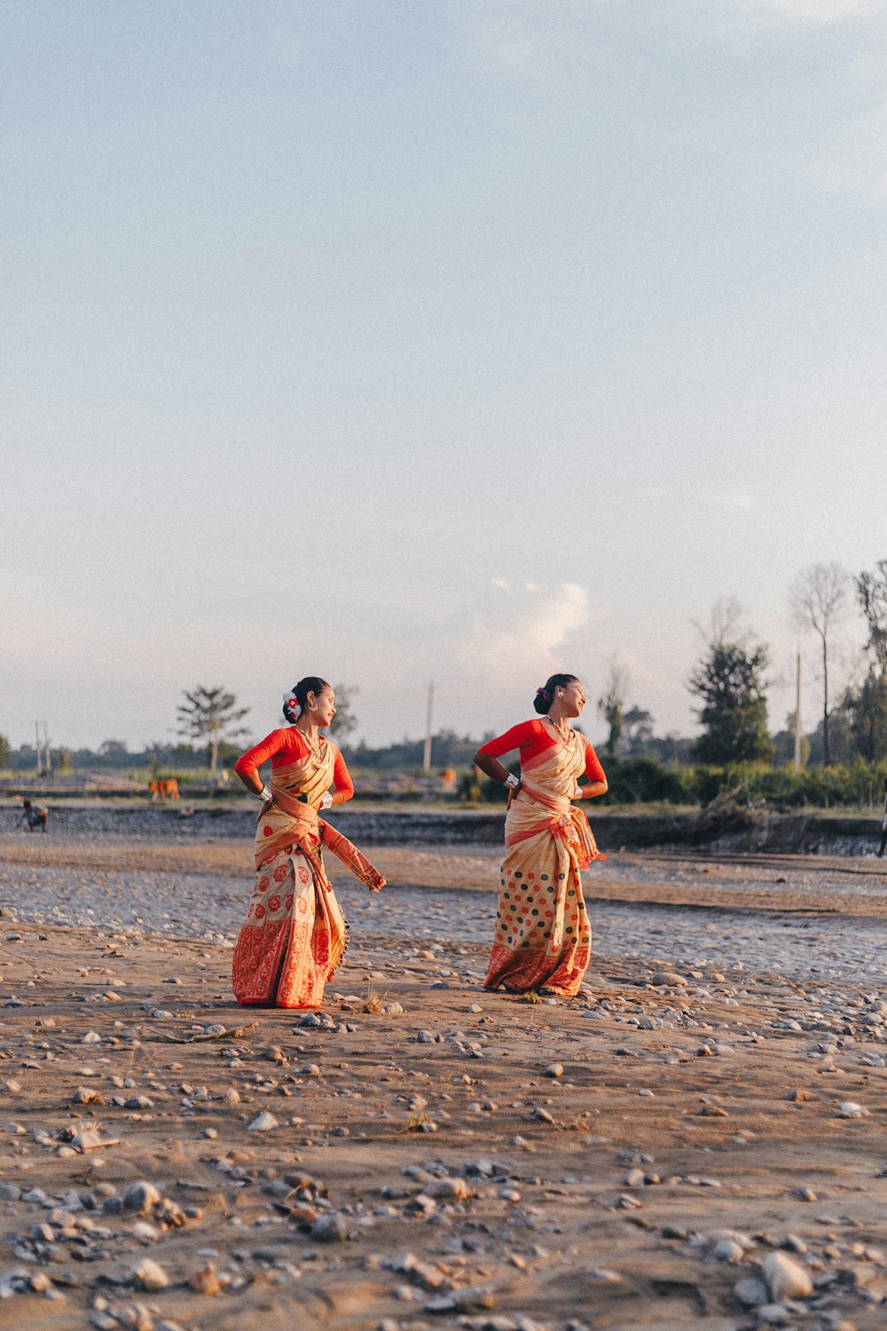 낮 동안 수역 근처의 갈색 모래 위를 걷는 2명의 여성