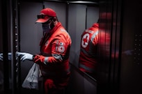 man in red and white jacket standing beside black wall