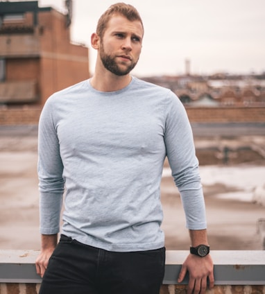 man in white long sleeve shirt and black pants standing on brown wooden fence during daytime