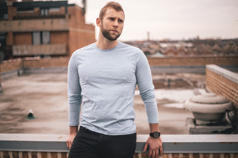 man in white long sleeve shirt and black pants standing on brown wooden fence during daytime