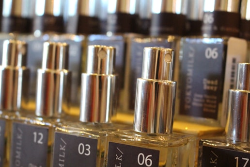 Several glass bottles with silver spray nozzles are arranged in rows. Each bottle is labeled with different numbers and text. The labels are dark with white fonts. The image focuses on the middle row of bottles with the numbers 03 and 06 clearly visible.