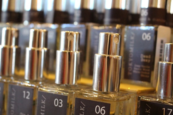 Several glass bottles with silver spray nozzles are arranged in rows. Each bottle is labeled with different numbers and text. The labels are dark with white fonts. The image focuses on the middle row of bottles with the numbers 03 and 06 clearly visible.