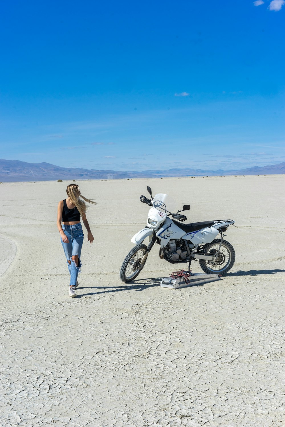 woman in black tank top and blue denim jeans standing beside black and white motorcycle on on on on on