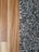 A close-up view showing the contrast between a smooth wooden floor and a textured, shaggy carpet. The left side features the warm tones and grain patterns of the wooden flooring, while the right side displays the irregular, intertwined fibers of a multi-toned black and gray carpet.