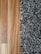 A close-up view showing the contrast between a smooth wooden floor and a textured, shaggy carpet. The left side features the warm tones and grain patterns of the wooden flooring, while the right side displays the irregular, intertwined fibers of a multi-toned black and gray carpet.