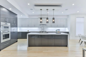 A modern kitchen with grey cabinets, a white island, and three pendant lights