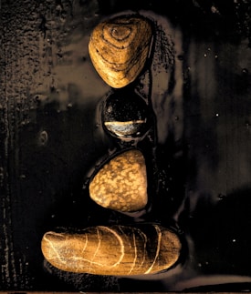Four stones with unique patterns are arranged in a vertical line on a glossy black surface, each stone displaying different earthy colors and textures.