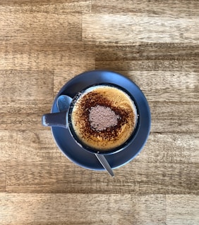 A cappuccino cup topped with foamy milk art and a sprinkle of cocoa on a saucer.