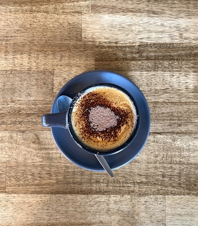 A cappuccino cup topped with foamy milk art and a sprinkle of cocoa on a saucer.