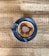 A cup of frothy cappuccino with cocoa powder sprinkled on top, placed on a saucer with a spoon, all set on a wooden table.