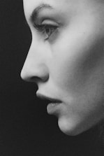 A high-contrast black and white image of a person's side profile with sharp focus on the facial features, particularly the eye and nose. The person appears to be looking forward with a calm and introspective expression.