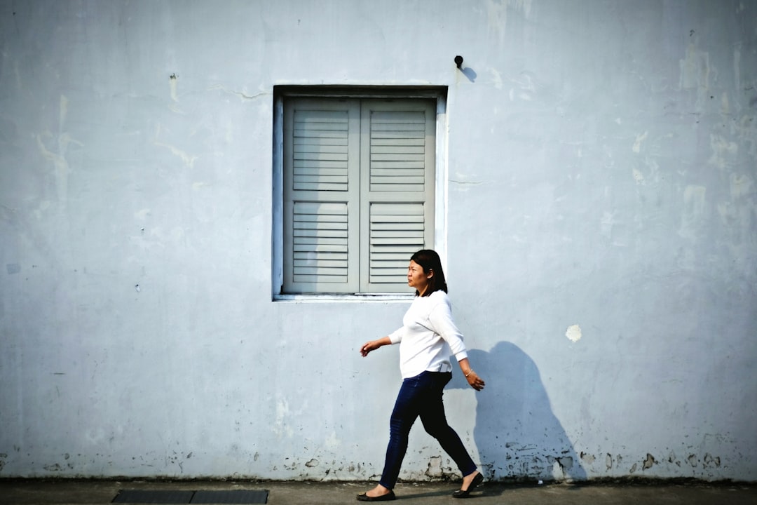 woman in white long sleeve shirt and black pants jumping near white wall during daytime