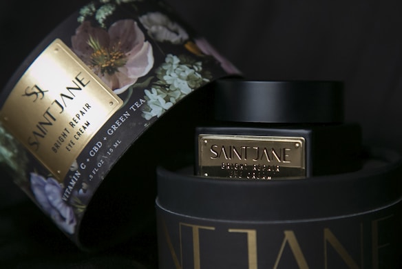 A luxury skincare product package with floral design, highlighting a Saint Jane Bright Repair Eye Cream. The box features elegant, muted colors with a touch of gold and a sophisticated floral pattern. The product emphasizes its ingredients such as Vitamin C, CBD, and Green Tea.