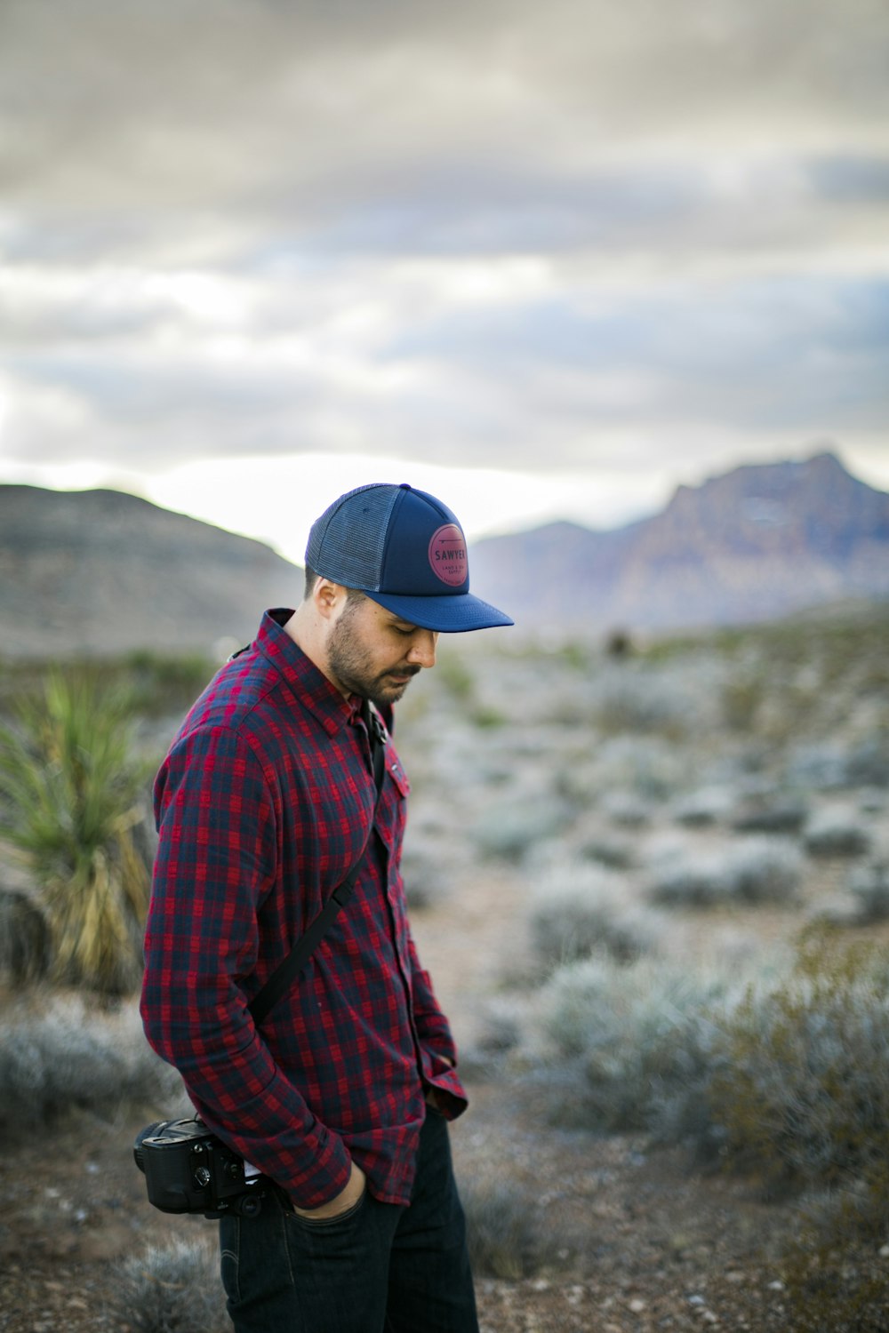 Hombre con camisa de vestir a cuadros rojos y negros y gorra ajustada azul de pie sobre hierba verde